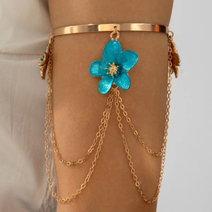 Close-up of golden upper arm bracelet with blue enamel flower and layered chain tassels