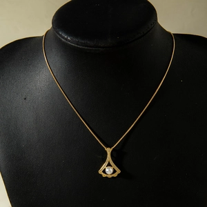 Detail of a fan-shaped gold pendant with a central pearl and crystals on a snake chain