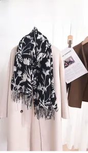 Détail d'une écharpe fleurie noire et blanche à longues franges sur un manteau beige