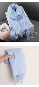 Detail of light blue knitted scarf texture featuring delicate fringe and soft cashmere-like fabric