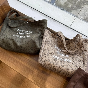 Detail of leopard print tote bags in green and beige with text print on wood stairs