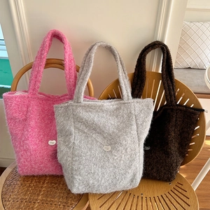Trois sacs cabas en peluche rose, gris et marron sur une chaise, style hiver doux