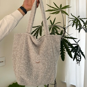 Détail d'un sac cabas en fausse fourrure grise avec un petit logo métallique en forme de cœur