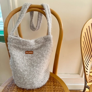 Detail of grey plush bucket bag with leather patch hanging on a wooden vintage chair