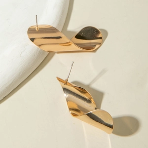 Gros plan de boucles d'oreilles dorées avec design ondulé sur un support minimaliste