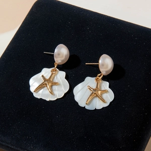 Detailed shot of bohemian gold starfish earrings with shells and pearls on black velvet