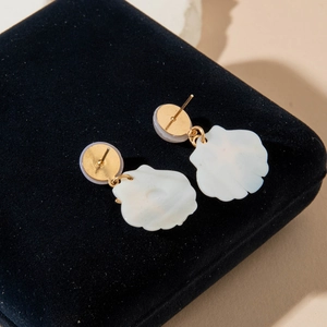 Detail of gold-plated geometric earrings with white textured shell-like pendants