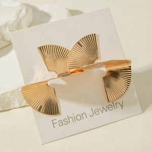 Détail de boucles d'oreilles dorées en forme d'éventail avec texture sur fond de pierre blanche
