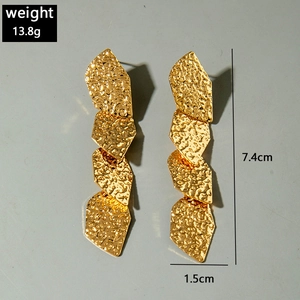 Détail de boucles d'oreilles pendantes géométriques dorées avec effet martelé et mesures