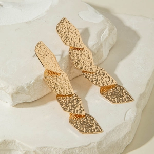 Détail de boucles d'oreilles pendantes dorées avec texture martelée sur maillons géométriques