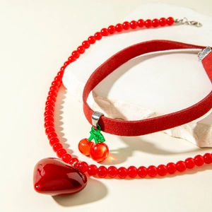 Détail du collier à perles rouges cœur et choker cerise sur support en pierre