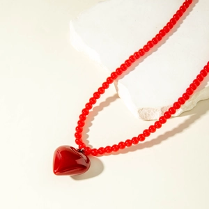 Détail du collier de perles rouges avec un pendentif cœur brillant sur une pierre