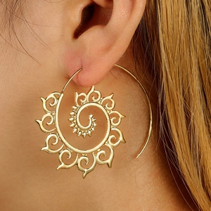 Macro detail of gold spiral hoop earrings with intricate tribal swirl patterns on model