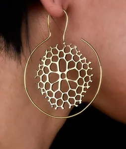 Detailed close-up of large golden teardrop earrings with a geometric hollow mesh pattern
