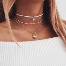 Close-up of layered gold necklace set with heart cross, pearls and crystal pendants