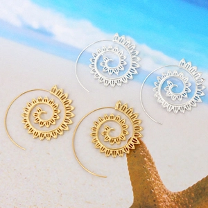 Detailed view of bohemian spiral leaf earrings in gold and silver on beach sand