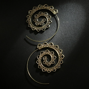 Close-up of vintage bronze spiral earrings with intricate floral cut-outs on leather
