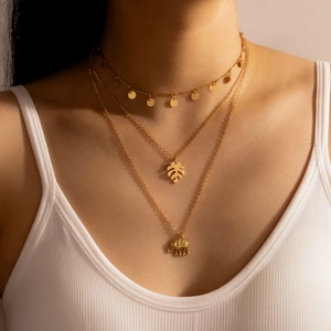 Detail of layered gold necklace featuring palm leaf and 3D elephant charms on a model