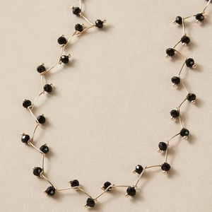 Detaillierte Makroansicht einer goldenen Wellenkette mit 2mm facettierten schwarzen Perlen