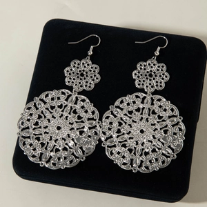Detailed close-up of large bohemian silver hollow floral earrings on black velvet