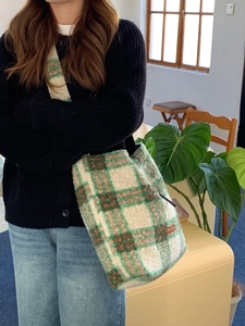 Close-up of green and brown plaid lamb wool shoulder bag with stitched leather label