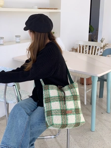 Detail of green plaid wool tote bag featuring a brown brand tag and adjustable drawstring