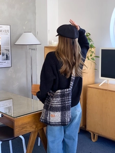 Back view of model wearing a plaid fleece tote bag with warm minimalist interior background