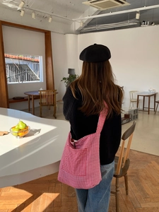 Detail view of large red plaid canvas crossbody bag worn by a model in a cozy room