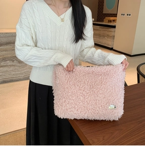 Détail de la texture en peau de mouton rose et logo métallique sur un sac en peluche doux