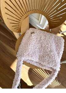 Détail de la texture d'un sac cabas en fausse fourrure rose sur une chaise en bois ensoleillée
