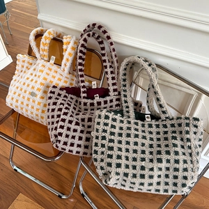 Macro detail of plush checkered tote bags featuring silver heart-shaped metal logo plates