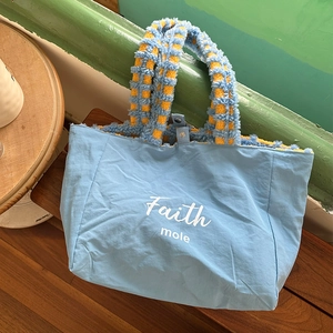 Detail of blue canvas tote bag with plush yellow checkerboard handle and Faith mole text