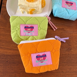Dettaglio di pochette trapuntate a cuore in arancione, verde e blu su piano di legno