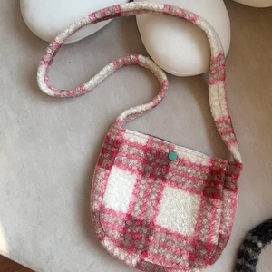 Close-up of pink plaid lamb wool crossbody bag with a green snap button closure