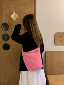 Pink plush faux fur bucket bag shown worn over the shoulder with a stylish outfit