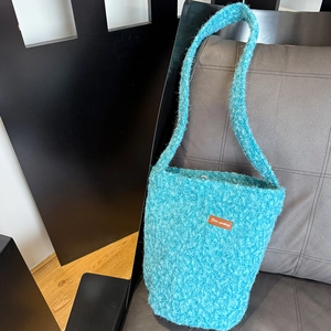 Detail view of turquoise plush bucket bag with brown leather Star-picking label and soft texture