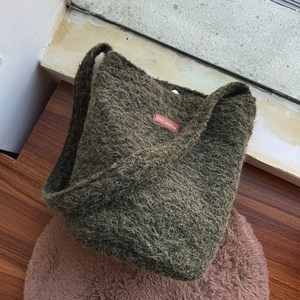 Close-up of forest green plush bucket bag showing curly faux fur texture and leather label