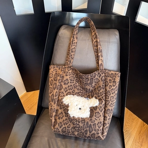 Close-up of leopard print faux suede tote bag with plush puppy embroidery on a leather chair