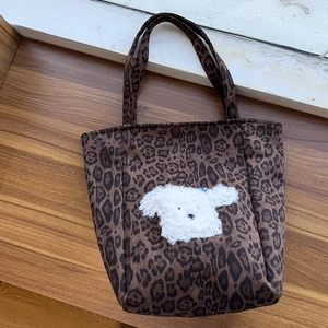 Detail of suede leopard print tote bag with cute plush puppy patch on wooden surface
