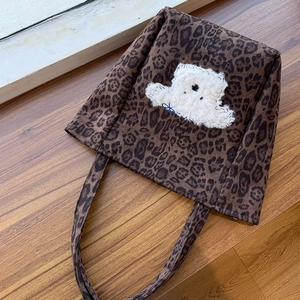 Detail of leopard print suede tote bag featuring a fuzzy white polar bear patch with blue bow