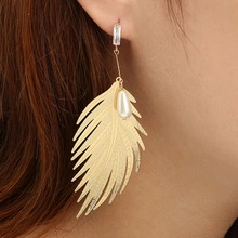 Detail von goldenem Federohrring mit Perle und Kristall an einem weiblichen Modell