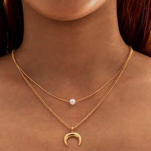 Gros plan d'un collier doré double rang orné d'une perle blanche et d'un pendentif demi-lune