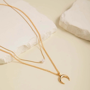 Détail d'un collier double rang doré avec perle blanche et pendentif demi-lune poli