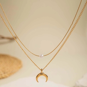 Gros plan d'un collier doré multicouche avec perle blanche et pendentif croissant de lune