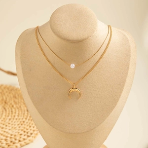 Détail d'un collier doré à deux rangs avec une perle blanche et un pendentif demi-lune