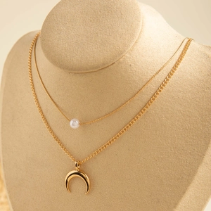 Détail d'un collier doré multicouche avec perle blanche et pendentif croissant poli