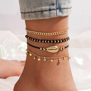 Detail of bohemian four-piece anklet set with alloy shells and black beads on white fabric