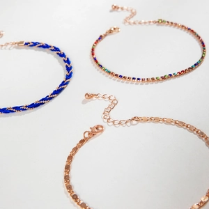 Detailed view of bohemian braided rope, colorful rhinestone, and gold disc layered anklets