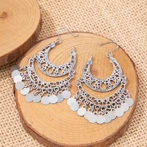 Macro view of boho hollow moon earrings with silver tassels on rustic wooden background