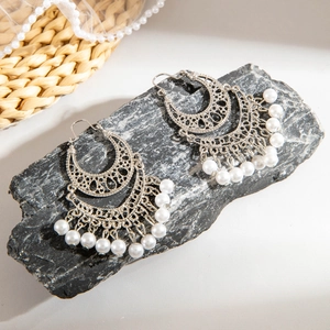 Detailed view of bohemian silver earrings with white pearls on a natural stone surface